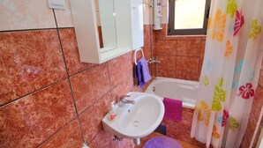 Een badkamer met een wastafel, spiegel, douche en een raam.