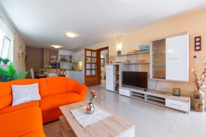 En moderne stue med en lys orange sofa, et træbord og et fladskærms-tv på et hvidt tv-møbel.