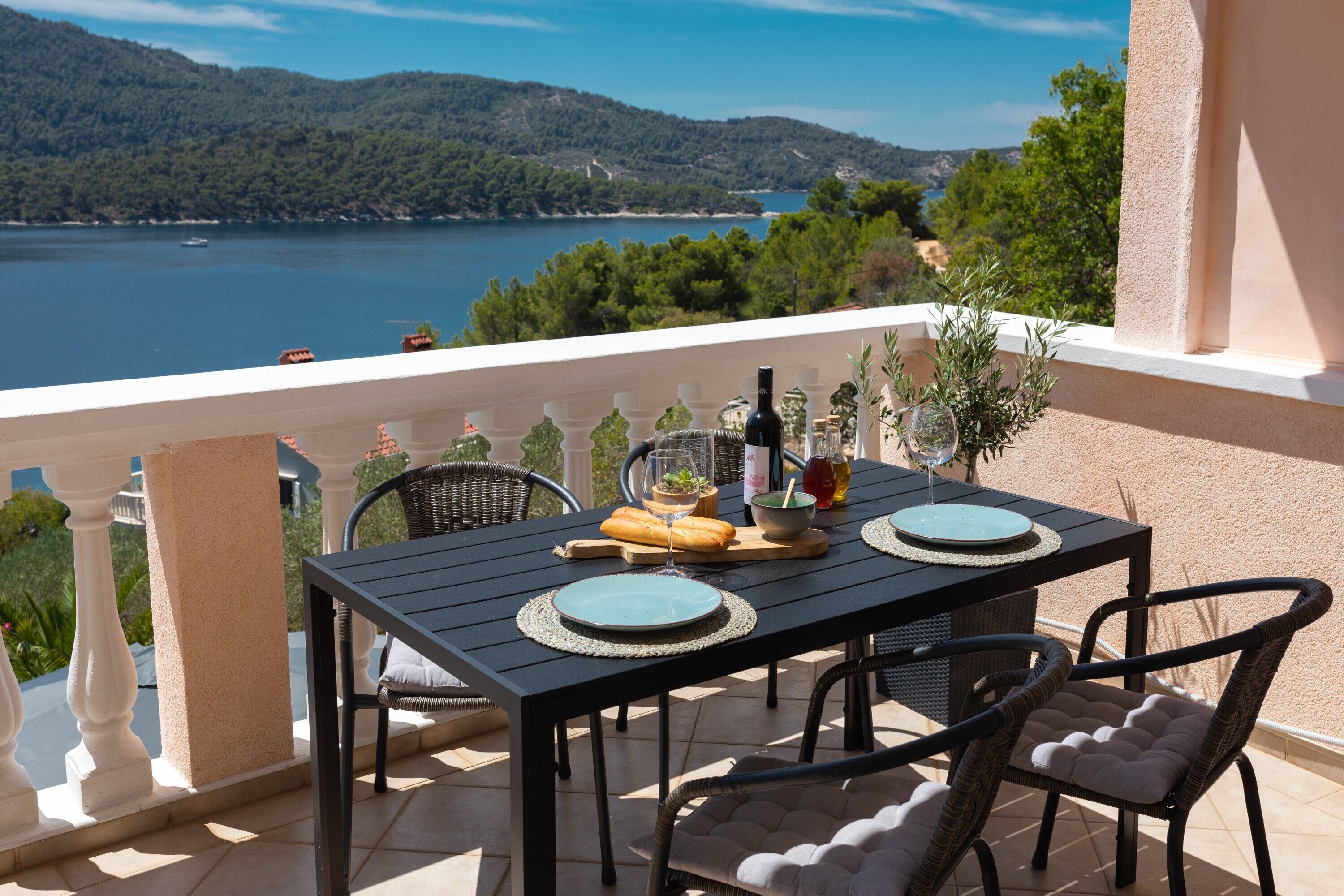 Ein Balkon mit Tisch für Zwei, mit Blick auf einen See und Hügel.