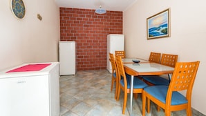 Een kleine kamer met een eettafel, stoelen, een koelkast en een metselwerk muur.