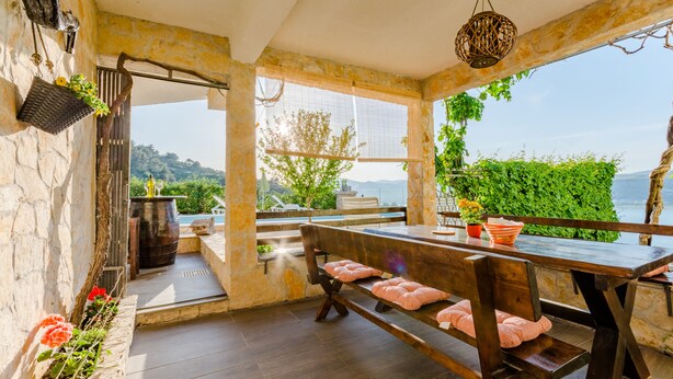 Un espace de restauration en plein air au charme rustique, avec un banc et une table en bois, des murs en pierre et une vue sur la mer.