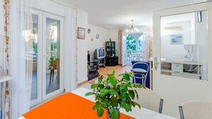 Un salon avec un téléviseur, une table à manger agrémentée d’un chemin de table orange et une plante en pot.