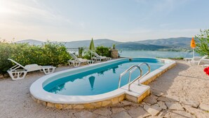 Une piscine bordée de pierres, entourée de chaises longues blanches et dont le fond est recouvert de petits galets.