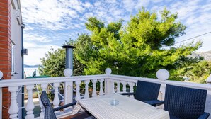 En balkon med et bord og stole, et hvidt gelænder og udsigt til træer og bjerge.