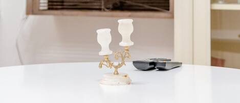Una mesa blanca redonda con dos candelabros blancos y un par de gafas de sol. Una silla de madera se ve parcialmente al frente.