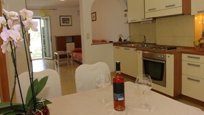 A modern kitchen with white cabinets, a dining table with two wine glasses, and a potted orchid. - Apartments Villa Muškat - Comfort Two Bedroom Apartment with Terrace (Supetar)