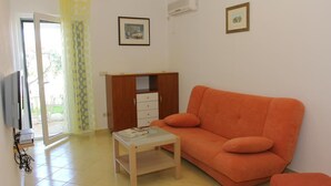 A living room with an orange sofa, a small wooden table, a TV, and a cabinet. - Apartments Villa Muškat - Comfort Two Bedroom Apartment with Terrace (Supetar)