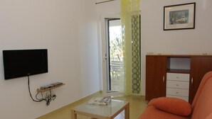 A living room with a flat-screen TV mounted on the wall, a small table with a book, an orange sofa, and a wooden cabinet with drawers. - Apartments Villa Muškat - Comfort Two Bedroom Apartment with Terrace (Supetar)