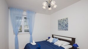 Une chambre à coucher comprenant un lit, une table de chevet, une lampe, une fenêtre avec des rideaux et une œuvre d’art murale.
