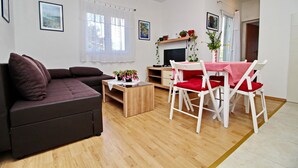A modern living room with a dark brown sofa, a wooden coffee table, and a dining area with white chairs and a red tablecloth.
