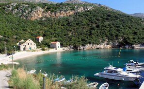 A coastal scene with a clear turquoise bay, boats docked, and traditional stone buildings on a hillside.