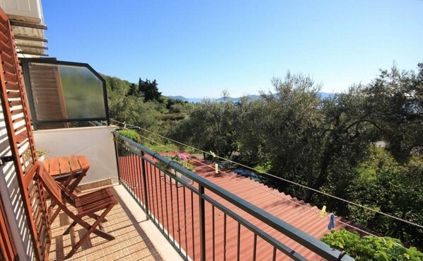 A balcony with a wooden bench, a metal railing, and a view of olive trees and hills.
