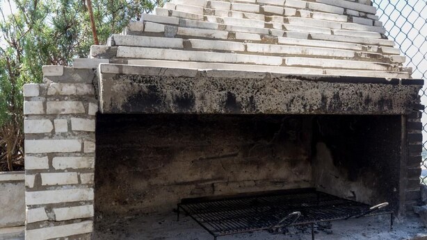 A brick-built outdoor grill with a metal grate and a chimney.