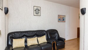 A black leather sofa with three cushions in a room with white textured walls, two framed pictures, and a wooden floor.