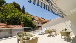 Una terraza en la azotea con mobiliario de mimbre, una mesa de vidrio y vistas de los edificios circundantes.