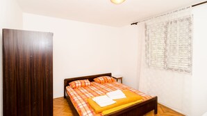 A bedroom with a bed, wooden headboard, and a window with patterned curtains. - Villa Peragić - Triple Room (Molunat)