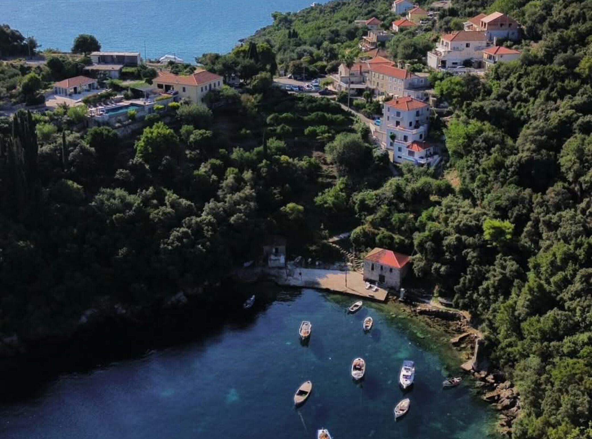 Vista aérea de un pueblo costero con casas, un mar azul cristalino y barcos anclados cerca de la orilla.