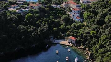 Vista aérea de un pueblo costero con casas, un mar azul cristalino y barcos anclados cerca de la orilla.