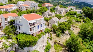 A coastal village with traditional stone houses, a prominent white building with balconies, and a mountainous backdrop. - Villa Kosa - Room with Balcony and sea View (Soba 2-Mira) (Brela)