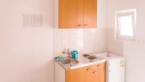A small kitchen with white tiles, wooden cabinets, a sink, a stove, and a window. - Apartmetns Franka Saplunara-One-Bedroom Apartment with Terrace and Sea View No2 (Saplunara)
