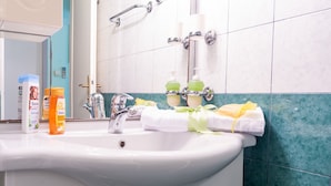 Ein Badezimmer mit einem weißen Waschbecken, grünen Fliesen, einem Spiegel und Toilettenartikeln.