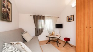 Ett mysigt rum med en soffa, ett litet bord med en flaska och glas, en tv och en garderob.