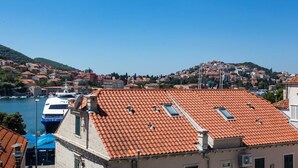A coastal town with terracotta-roofed buildings, a marina with boats, and a hilltop settlement in the background.