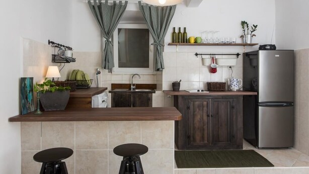 A modern kitchen with a central island, dark wooden cabinets, a stainless steel refrigerator, and a hanging light fixture.