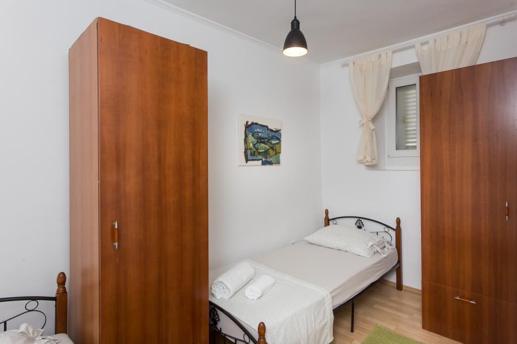 A bedroom with a single bed, wooden wardrobe, and a painting on the wall.