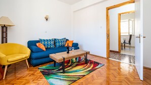 Un salon moderne avec un canapé bleu, un fauteuil jaune, une table basse en bois et un tapis coloré.