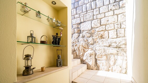Un couloir étroit avec un mur en pierre, une étagère ornée d’objets décoratifs et une lanterne.