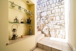 A narrow hallway with a stone wall, a shelf with decorative items, and a lantern.