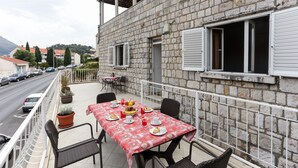 Un balcon avec une table préparée pour le petit-déjeuner, donnant sur une rue bordée de voitures garées et sur laquelle on aperçoit des bâtiments au loin.