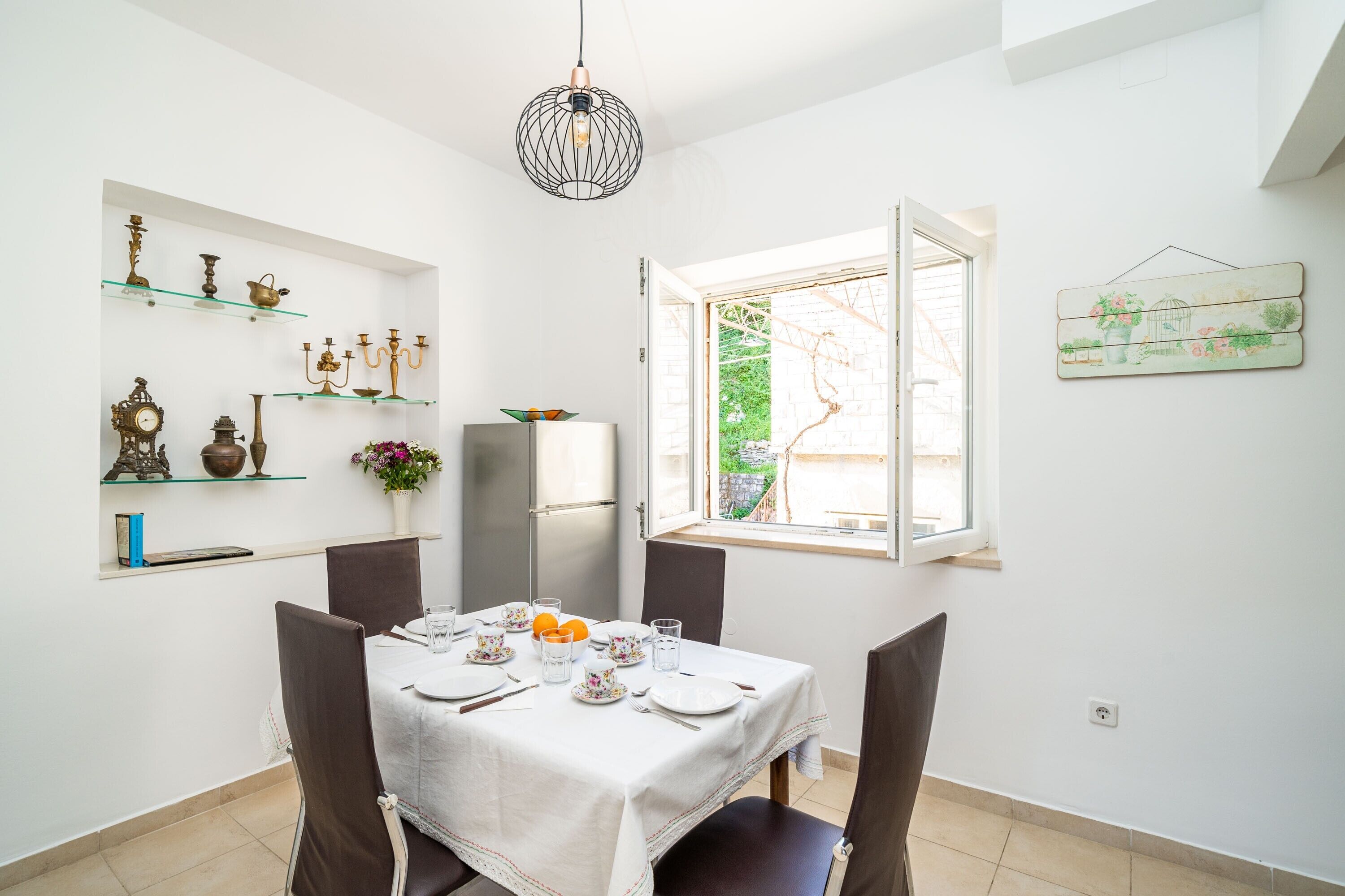 A dining area with a table set for four, a refrigerator, and decorative items on shelves.