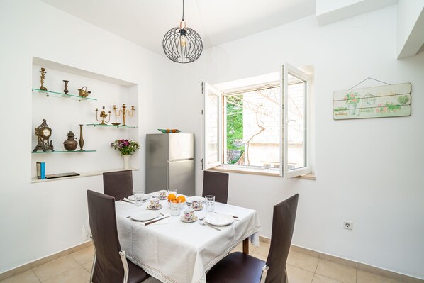 A dining area with a table set for four, a refrigerator, and decorative items on shelves.