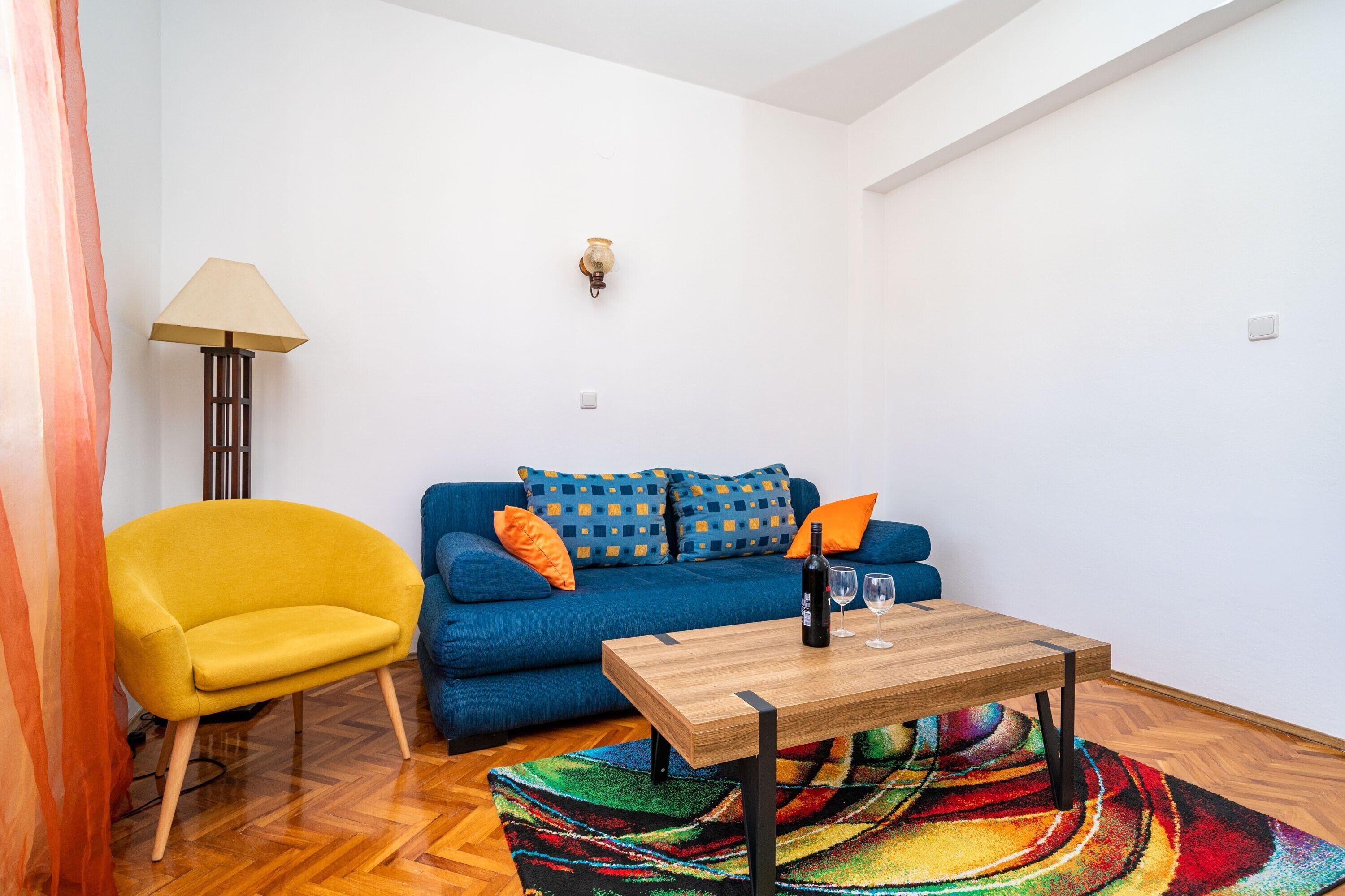 Una sala de estar moderna con un sofá azul, un sillón amarillo, una mesa de centro de madera y una alfombra colorida.
