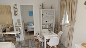A room with a bed, a small table with chairs, a white cabinet with glassware, and a window with curtains. - Apartments Mediterranean House - Two Bedroom Apartment with Terrace (Klek)