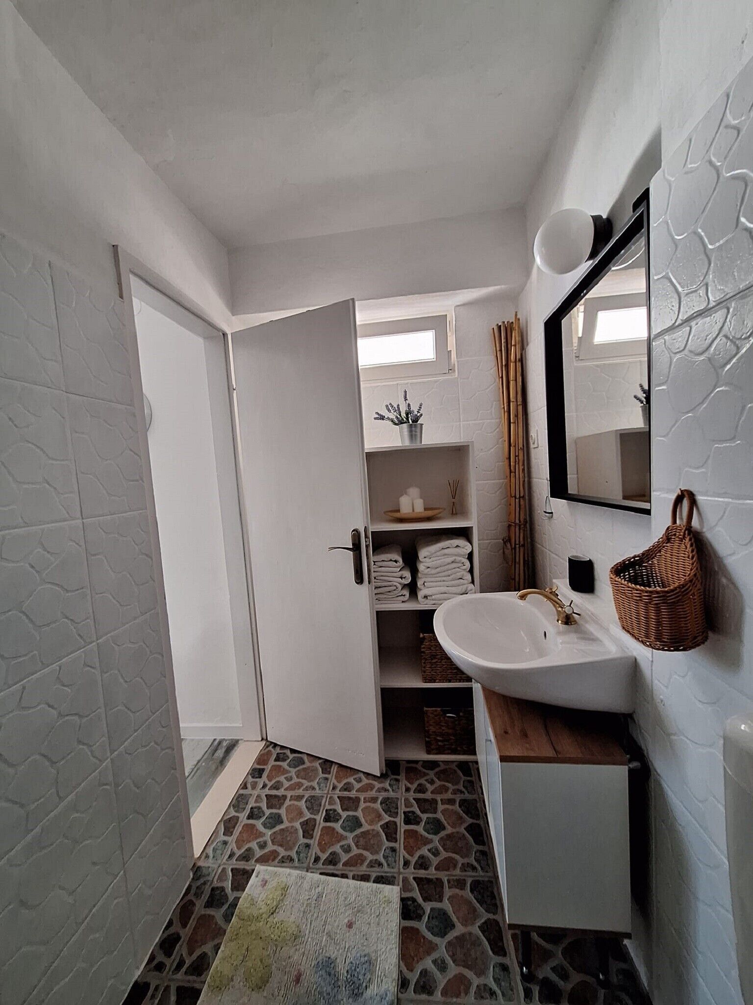 Un baño con lavamanos blanco, un espejo y un perchero. Hay una puerta que da a otra habitación.