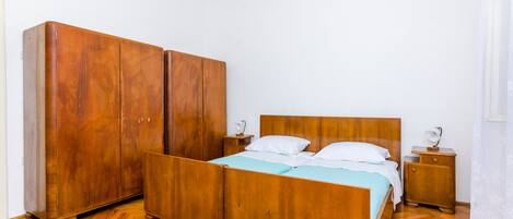 A bedroom with a wooden bed, a wardrobe, a nightstand, and a bedside table.