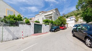 Eine enge Straße mit parkenden Autos, einem verschlossenen Eingang und Gebäuden mit Balkonen.
