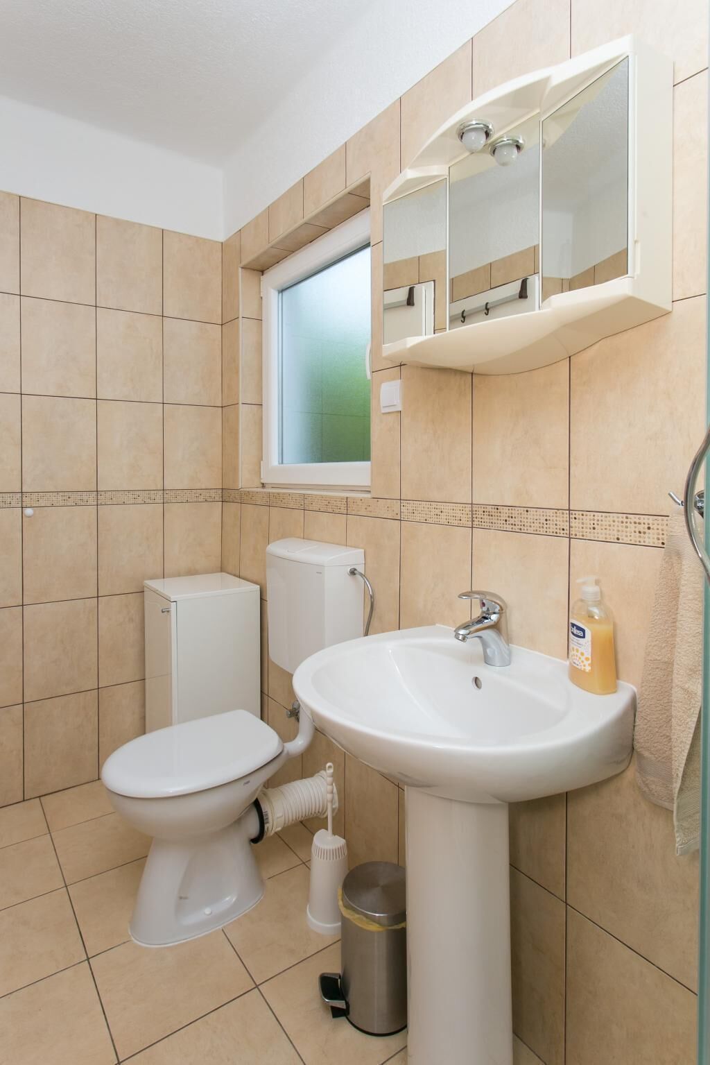 A bathroom with a toilet, sink, and window.