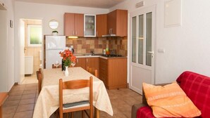 A compact kitchen with wooden cabinets, a refrigerator, and a dining area with a table and chairs.