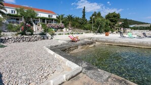 A coastal property with a swimming pool, a stone retaining wall, and a red-roofed building with a balcony.