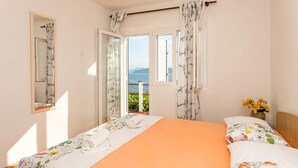 A bedroom with a bed, a window with curtains, a mirror, and a view of the sea.