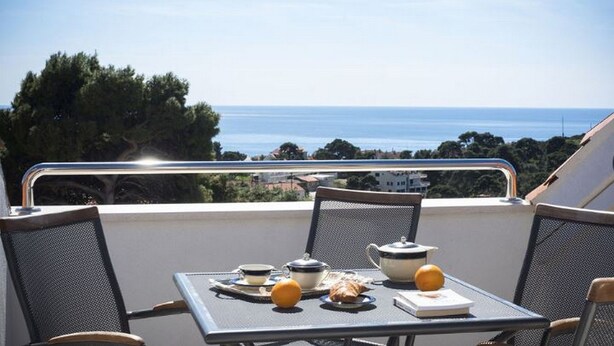 Un balcon avec une table préparée pour le petit-déjeuner, offrant une vue sur la côte.
