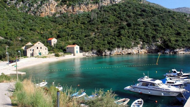 A coastal village with stone buildings, a clear turquoise sea, and boats docked at the shore.