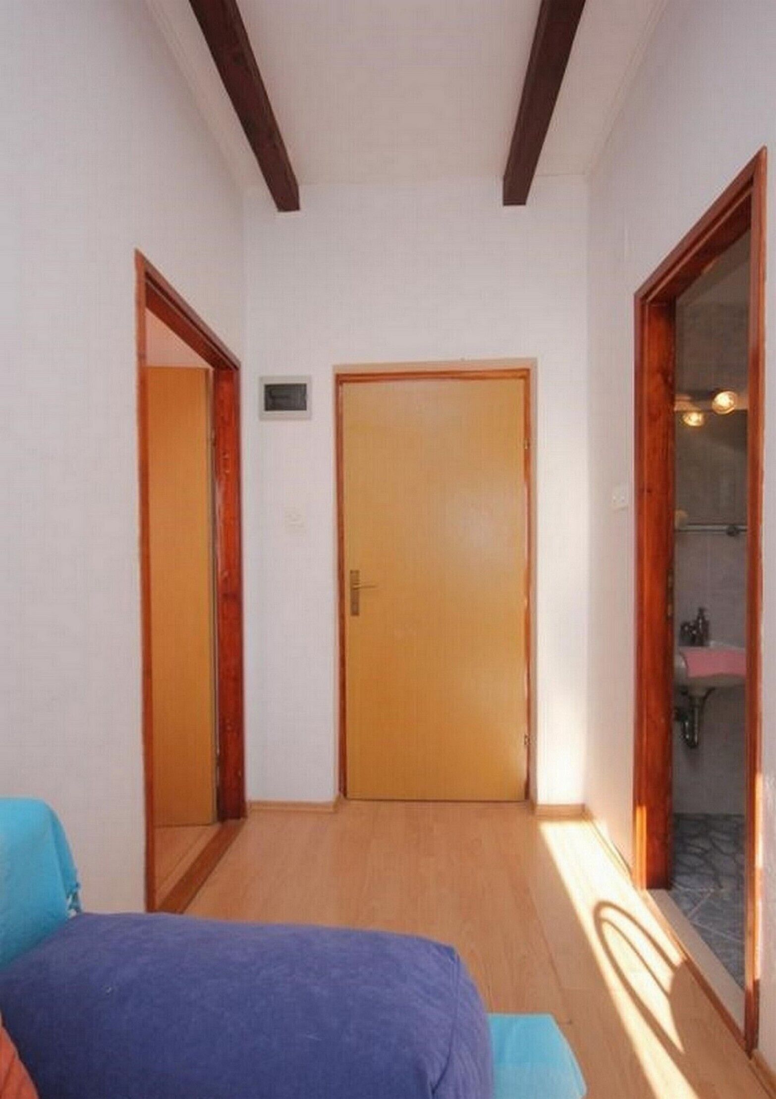 A narrow hallway with a wooden door at the end, a small window, and a bathroom visible through a glass door.