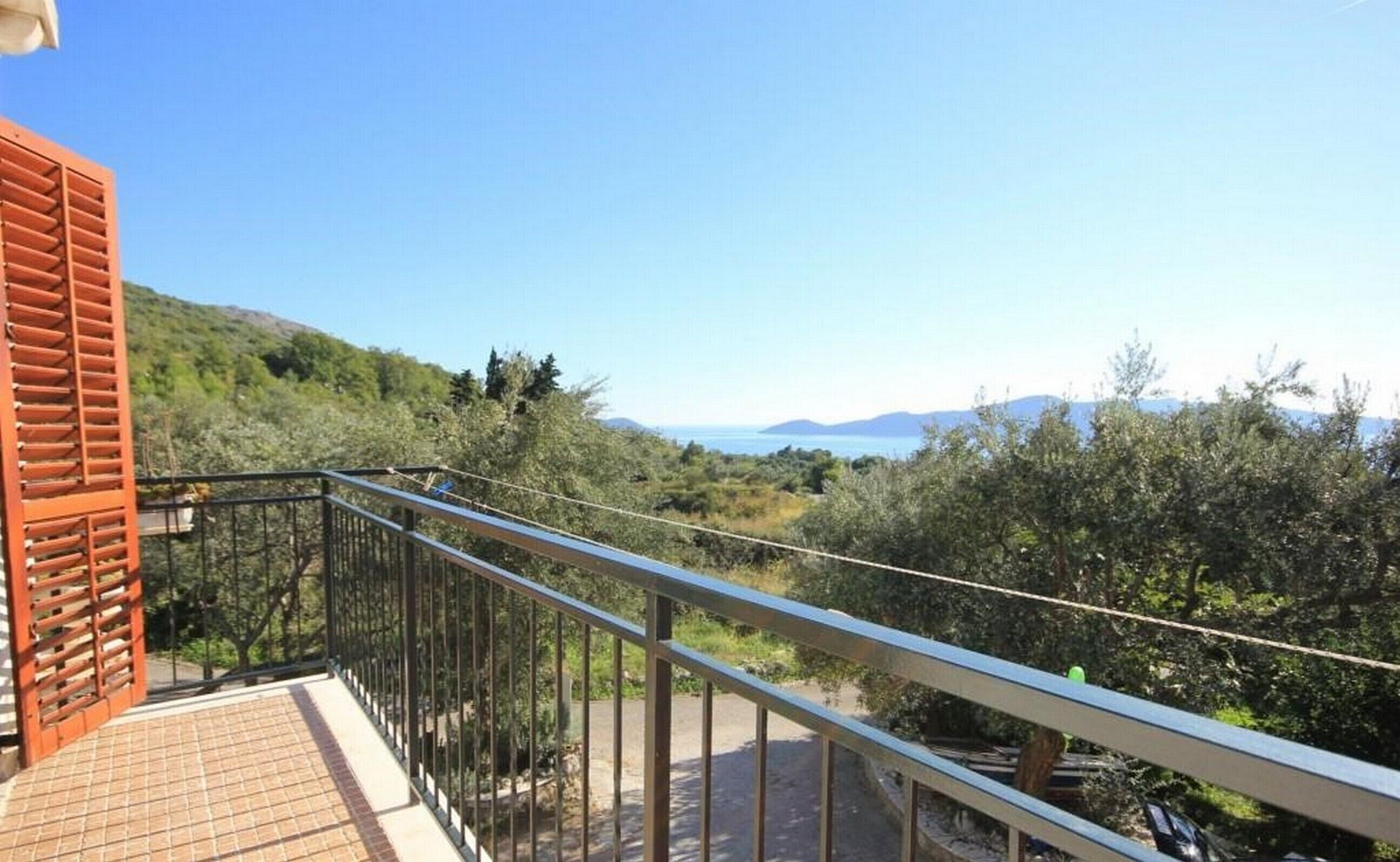 A balcony with a metal railing overlooking a mountainous landscape and a body of water.