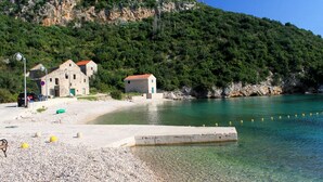 A coastal area with stone buildings, clear turquoise water, and a pebbled beach.