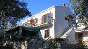 A two-story building with a balcony, a stone wall, and a staircase leading to the entrance.